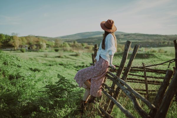 Sustainable fashion and eco-friendly wardrobes for women, A woman enjoys the peaceful rural landscape in Bălți, Moldova, leaning on a rustic wooden fence.